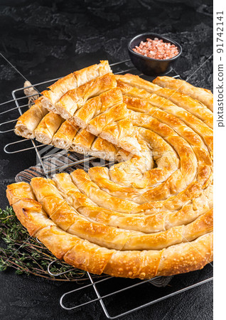 Turkish Tepsi Boregi, Round Borek cheese pie on kitchen board. Black background. Top view Turkish Tepsi Boregi, Round Borek cheese pie on kitchen board. Black background. Top view 91742141