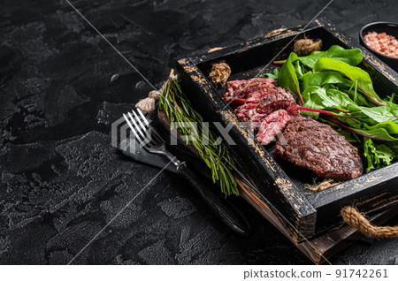 BBQ roasted flank steak in wooden tray with vegetable salad. Black background. Top view. Copy space BBQ roasted flank steak in wooden tray with vegetable salad. Black background. Top view. Copy space 91742261