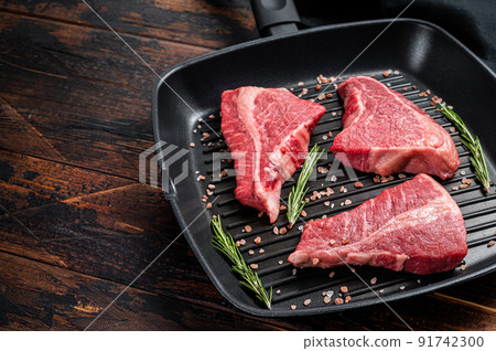 Raw sirloin beef steak, Rump steak cut on a grill skillet. Wooden background. Top view. Copy space 91742300