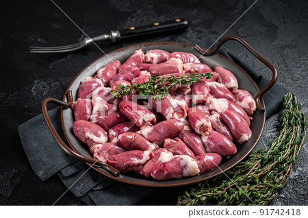 Raw chicken hearts in a steel tray with thyme. Black background. Top view 91742418