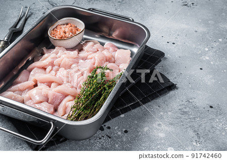 Diced raw chicken breast fillets in steel tray. Gray background. Top view. Copy space 91742460