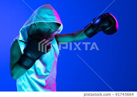 Stylish boy, beginner boxer training isolated over blue background in neon light. Concept of sport, fashion, studying, achievements, skills. Stylish boy, beginner boxer training isolated over blue background in neon light. Concept of sport, fashion, studying, achievements, skills. 91743664