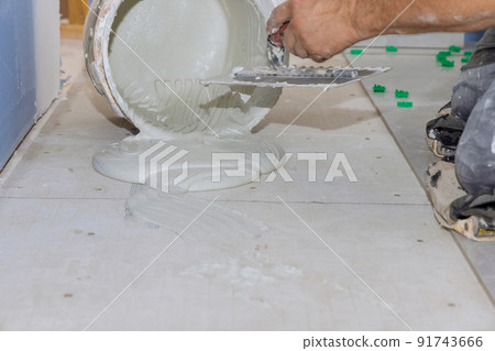 In preparation for laying floor tiles, troweling mortar applies adhesive to a concrete floor In preparation for laying floor tiles, troweling mortar applies adhesive to a concrete floor 91743666