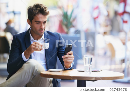 Expresso break. Shot of a young businessman reading a text while sitting at an outdoor cafe. 91743678