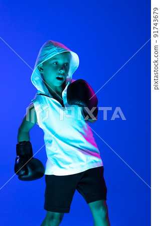 Stylish boy, beginner boxer training isolated over blue background in neon light. Concept of sport, fashion, studying, achievements, skills. 91743679