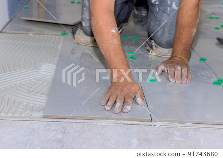 The placement of ceramic floor tiles on an adhesive surface with home construction workers The placement of ceramic floor tiles on an adhesive surface with home construction workers 91743680