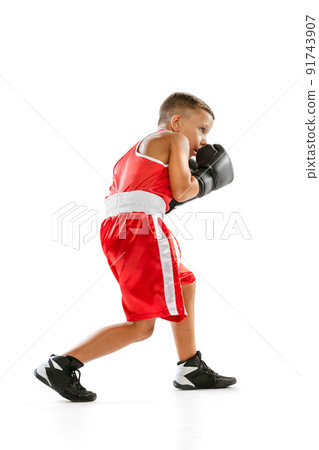 Portrait of active boy, beginner boxer in sports gloves and red uniform isolated on white background. Concept of sport, movement, studying, achievements, lifestyle. 91743907