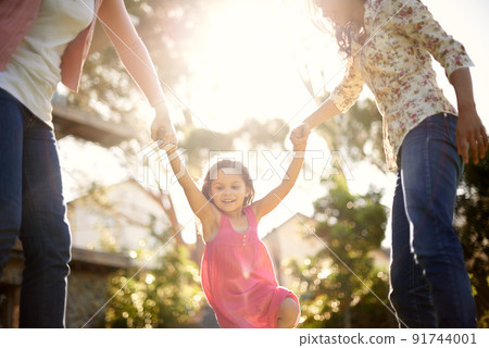 Having so much fun with her family. A cute little girl being swung by her mother and grandmother in the garden. 91744001