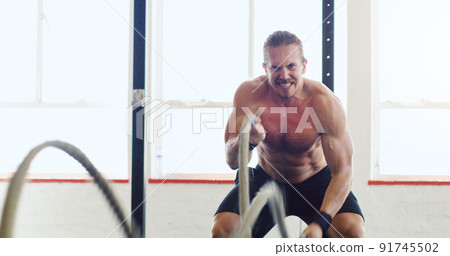 Maximum effort gets maximum results. Shot of a young man working out with battle ropes in a gym. Maximum effort gets maximum results. Shot of a young man working out with battle ropes in a gym. 91745502