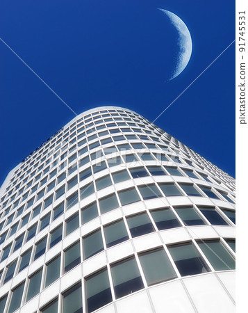 Half a moon over a building skyscraper, shining in bright blue sky. Below the crescent of quarter moon over a tall modern structural architecture, foreboding doomed capitalism or an economical crisis Half a moon over a building skyscraper, shining in bright blue sky. Below the crescent of quarter moon over a tall modern structural architecture, foreboding doomed capitalism or an economical crisis 91745531