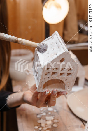 A master ceramist holds a clay product in his hands. Making a ceramic candle holder from clay. The process of coating the candlestick with glaze. 91745589