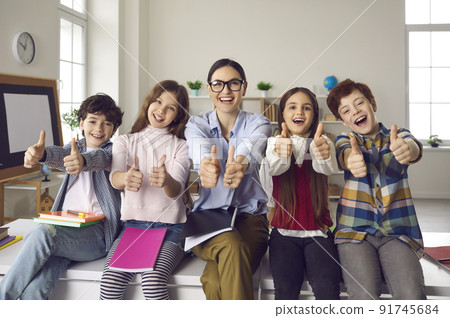 Happy smiling teacher with pupils group giving thumbs up portrait in schoolroom 91745684