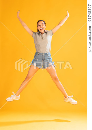 Portrait of beautiful young girl in casual outfit jumping, posing isolated over yellow studio background. Happiness 91748307