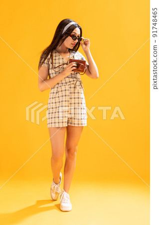 Portrait of beautiful stylish girl taking photo with vintage camera isolated over yellow studio background 91748465