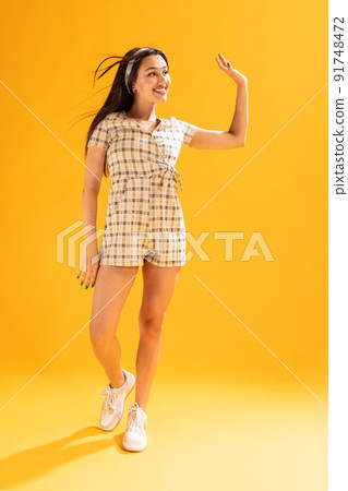 Portrait of beautiful young girl in stylish summer outfit posing, waving isolated over yellow studio background 91748472