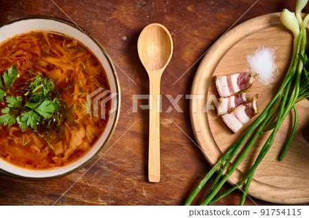 Served bowl with traditional Ukrainian Borscht, wooden board with sliced bacon, onion and salt on wood table background. Served bowl with traditional Ukrainian Borscht, wooden board with sliced bacon, onion and salt on wood table background. 91754115