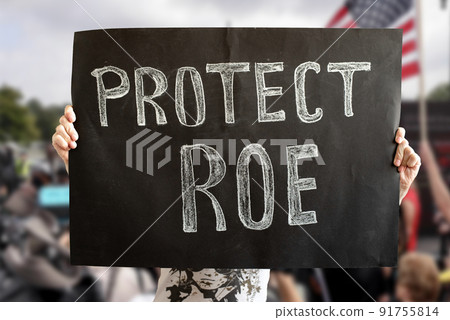 A woman's hands hold a Protect ROE banner. a woman stands up for her rights with a banner at a rally. The concept of protests in the United States. Fighting for the rights of women and feminists. Los 91755814