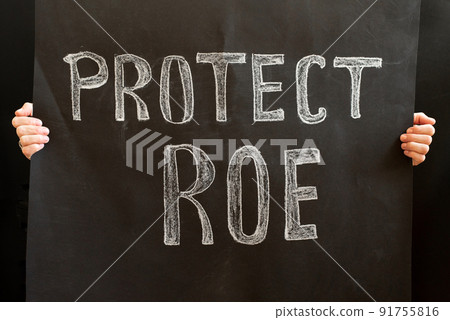 A woman's hands hold a Protect ROE placard. a woman stands up for her rights with a placard. The concept of protests in the United States. Women's rights and feminists fight for their rights A woman's hands hold a Protect ROE placard. a woman stands up for her rights with a placard. The concept of protests in the United States. Women's rights and feminists fight for their rights 91755816