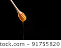 Shiny golden honey dripping off of a spoon into a wooden bowl with black background. Honey spoon on a black background. Blank space for text 91755820