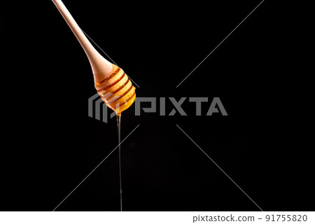 Shiny golden honey dripping off of a spoon into a wooden bowl with black background. Honey spoon on a black background. Blank space for text 91755820