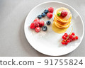 Pancakes on a white plate on a light background with berries and honey. empty space for text. 91755824