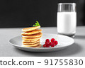Mini pancakes with blueberries and raspberries. American breakfast on a dark background. Healthy eating for the whole family. Homemade pancakes with berries. A glass of milk in the background 91755830