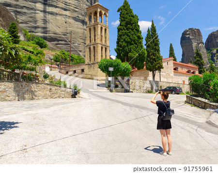 a tourist walking and takes pictures on a smartphone near the bell tower of Byzantine Church of the Assumption of Virgin Mary in Kalabaka 91755961