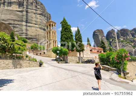 a tourist walking and takes pictures on a smartphone near the bell tower of Byzantine Church of the Assumption of Virgin Mary in Kalabaka 91755962
