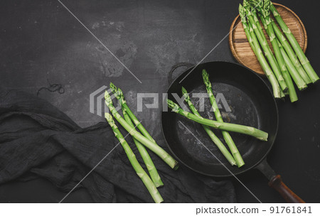 Fresh green asparagus in a round cast iron pan on a black table Fresh green asparagus in a round cast iron pan on a black table 91761841