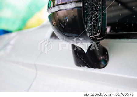 Modern white car covered by a liquid soap foam while washing. Side mirror of the modern car with a soap bobble and form close up with copyspace. 91769575