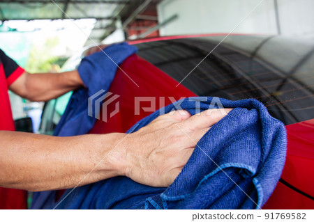 Man worker using microfiber wiping a water outside the modern red car after washing. Workman wiping and removing a scratches on the surface of the red car. Car care concept. 91769582