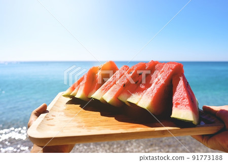 Juicy slices of watermelon on plate. In the background the sea and the beach. Red watermelon, fresh Juicy slices of watermelon on plate. In the background the sea and the beach. Red watermelon, fresh 91773188