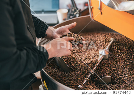 Male barista checks the quality of roasting coffee beans on small factory. Close-up Male barista checks the quality of roasting coffee beans on small factory. Close-up 91774443