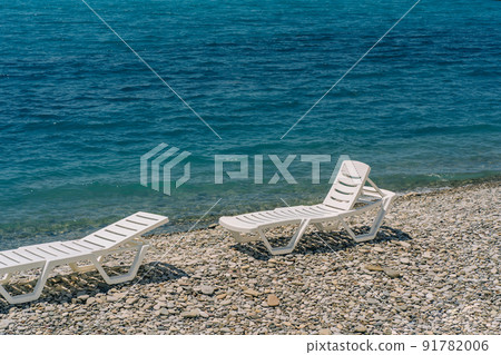 Pair of sun loungers at pebble beach, perfect vacation. 91782006