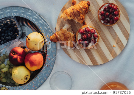 Flat Lay of Picnic Set, Fruits and Cakes with Croissants Laid Up on the Plaid at Sunset 91787036
