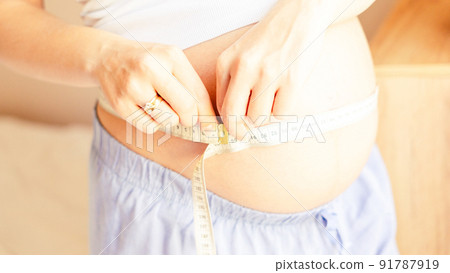 Belly size pregnancy woman measure. Happy young pregnant woman with tape measuring belly. Therapy, healthcare, motherhood concept. 91787919