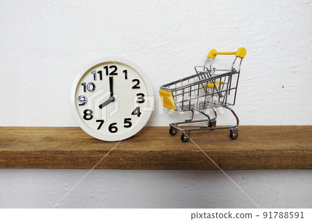 White alarm clock and Yellow mini shopping trolley cart on wooden shelves 91788591