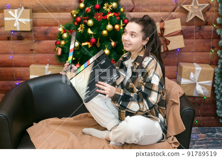 Teen girl with movie director's clapperboard near the Christmas tree with gifts Teen girl with movie director's clapperboard near the Christmas tree with gifts 91789519