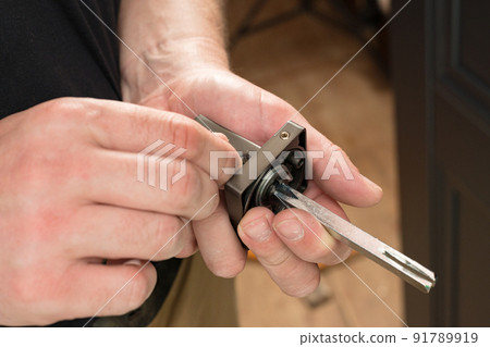 The craftsman holds a door handle and a hex key in his hands, installing a door handle. The craftsman holds a door handle and a hex key in his hands, installing a door handle. 91789919