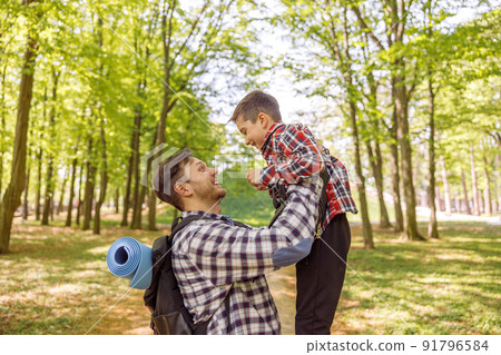 Cheerful Caucasian man holding his small cute son in hands high. Rising kid. At forest. 91796584