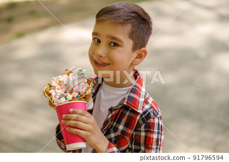 Portrait of cute small Caucasian boy with sweet waffle in hands. Kid smiling with fast food. 91796594