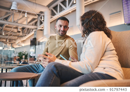 Happy young couple talking while sitting in VIP lounge of airport departure terminal waiting to board flight Happy young couple talking while sitting in VIP lounge of airport departure terminal waiting to board flight 91797443