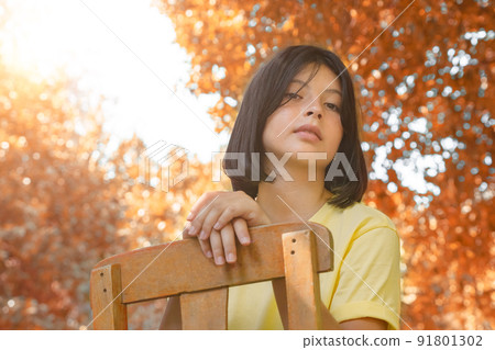 A young girl sits on an old wooden chair and enjoys the fresh air. A young girl sits on an old wooden chair and enjoys the fresh air. 91801302