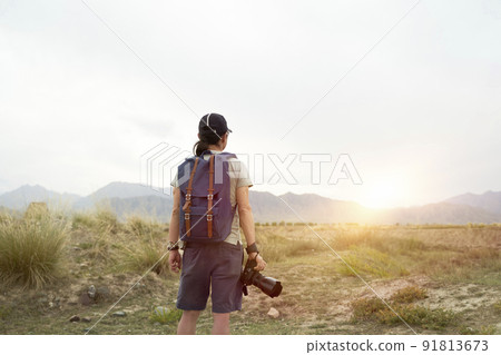 rear view of an asian photographer looking at view in the morning sunlight with camera in hand rear view of an asian photographer looking at view in the morning sunlight with camera in hand 91813673