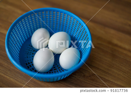 4 white chicken eggs in blue plastic basket on wood floor. 1 of 4 Chicken is ready to break out the egg shell from inside. 4 white chicken eggs in blue plastic basket on wood floor. 1 of 4 Chicken is ready to break out the egg shell from inside. 91817736