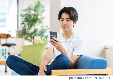 A young man looking at his smartphone in the living room A young man looking at his smartphone in the living room 91821081