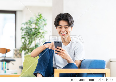 A young man looking at his smartphone in the living room A young man looking at his smartphone in the living room 91821088