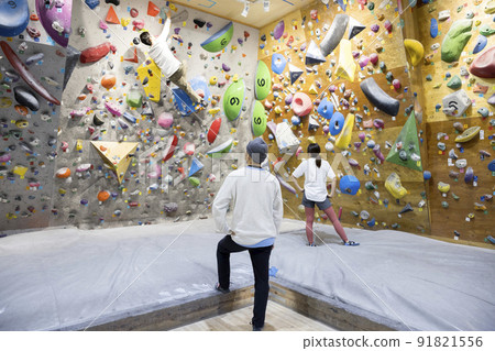 A companion watching over a young man bouldering 91821556