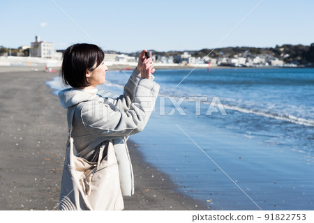 A woman taking a picture of the winter coast with a smartphone 91822753