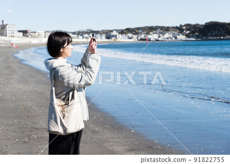 A woman taking a picture of the winter coast with a smartphone 91822755